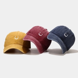 Detail of embroidered smile icons on vintage washed cotton baseball caps in three colors
