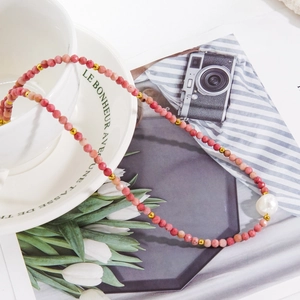 Detailed close-up of beaded necklace with faceted rhodochrosite and baroque pearl on a magazine