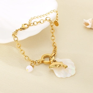 Close-up of golden steel bracelet with dolphin, pearl, and shell charms on beach scene