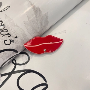 Macro shot of red lip-shaped hair clip with sparkling white rhinestone on decorative page