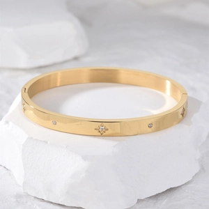Polished gold bangle with starburst engraving and crystals on white stone base