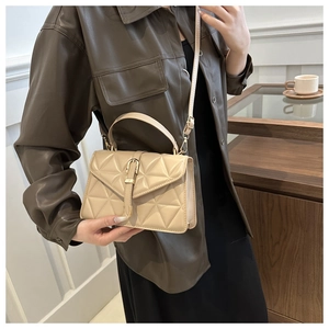 Detail of beige quilted PU leather crossbody bag worn by model with brown jacket