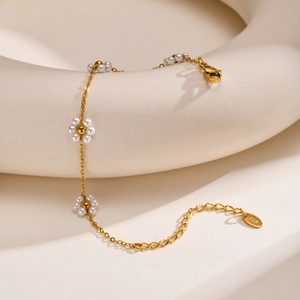 Close-up of gold chain bracelet with pearl daisy charms and K18 engraved tag detail