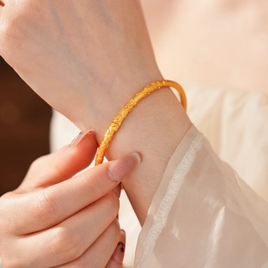 Close-up of vintage brushed gold bangle with detailed floral embossing on woman's wrist