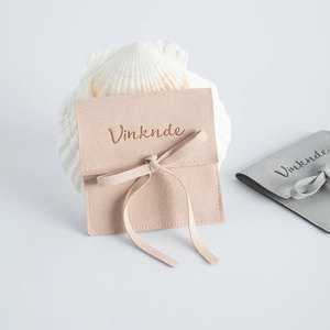 Pink and gray microfiber suede jewelry pouches with a ribbon bow on a shell stand