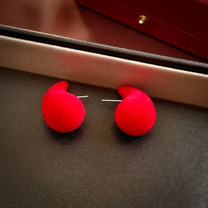 Macro detail of red flocked teardrop stud earrings with silver needles on leather surface