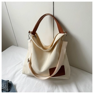 Detail of canvas tote bag featuring brown leather handles and a versatile shoulder strap