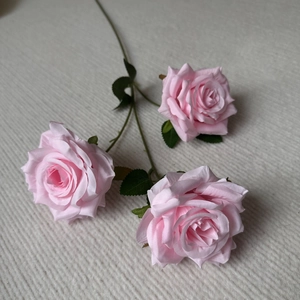 Close-up of three pink silk rose heads with realistic textures and lush green leaves