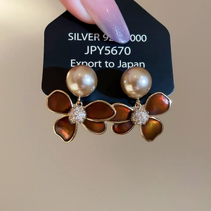 Detailed macro of 18k gold plated flower stud earrings with champagne pearl and zircons