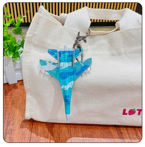 Detail view of mini camouflage fighter jet keychain clipped on a canvas bag