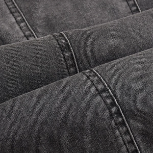 Gros plan sur le tissu denim gris foncé lavé montrant la texture et les coutures de qualité