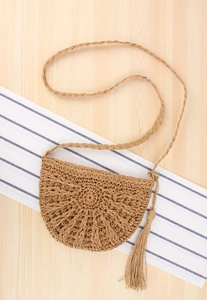 Detail of handmade woven straw crossbody bag with decorative fringe on a seaside table