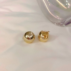 Detailed view of French style minimalist golden sphere earrings on a soft fabric backdrop