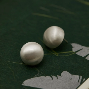 Detail shot of silver brushed metal hemispherical earrings on dark textured paper