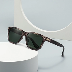 Classic round sunglasses in dark gray tortoiseshell frame with green lenses on white stand