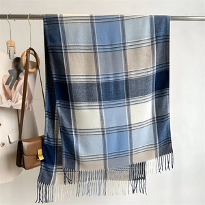 Detailed view of checkered scarf with fringe hanging by a leather handbag
