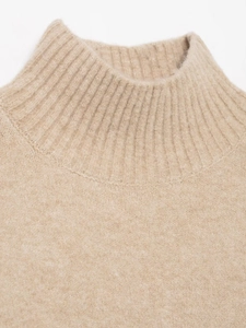 Gros plan sur un pull en maille abricot avec col montant côtelé et texture délicate
