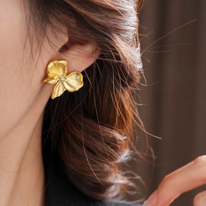 Close-up of a model wearing a gold flower earring with crystal center and wavy petals