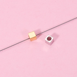Detail of 4mm stainless steel cube beads in gold and silver finish on textured paper