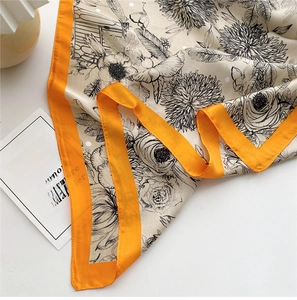 Close-up of a floral silk square scarf with orange border and black botanical patterns