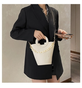 Detail of white bucket bag with circular handle and thick chain on black blazer