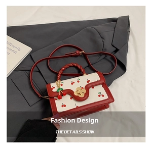 Detail of cherry print handbag featuring metal flower clasp and red rope handle texture