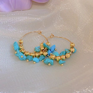 Detail of bohemian gold hoop earrings with turquoise stones on elegant mesh background