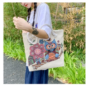Close-up of owl and floral embroidery on a cream canvas tote bag with cotton rope strap