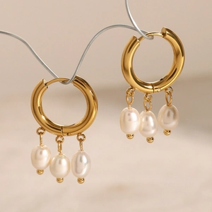 Detailed view of gold hoop earrings featuring three white pearls on a beige background