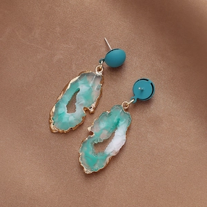 Close-up of green irregular resin earrings with gold edges on brown fabric background