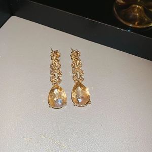 Close-up of champagne teardrop crystal earrings with gold plating on a gray display tray