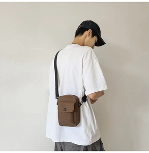 Dark brown canvas crossbody bag with adjustable strap worn by model in casual style