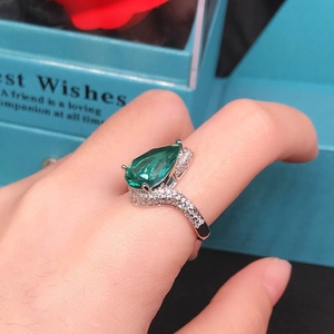 Detailed shot of large pear-cut emerald stone ring on hand with elegant gift packaging