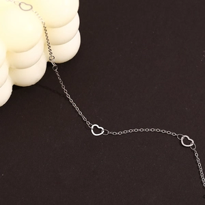 Detail of silver heart-shaped cutout links on a minimalist delicate chain anklet