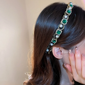 Detailed close-up of a vintage headband with green gemstones and white pearls on a model