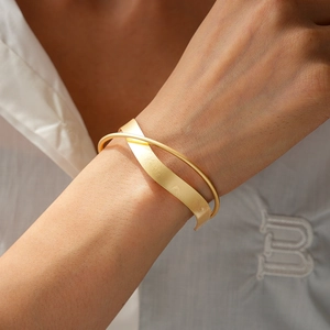 Detail of minimalist golden double-layered cross cuff bracelet with matte brushed texture