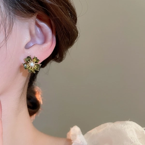 Detail view of flower stud earring with green crystals on ear of a fashion model
