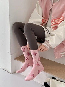 Pink crew socks with black heart patterns worn by a model on wooden steps