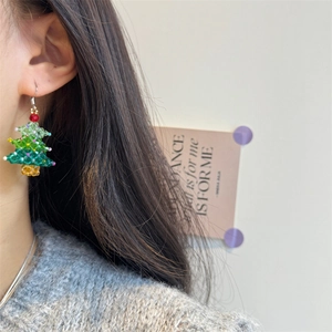 Close-up of handmade beaded Christmas tree earrings with a red bow on model ear