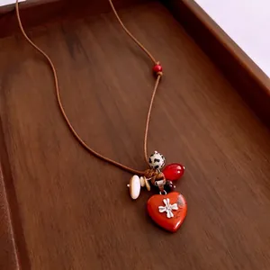 Collier pendentif cœur rouge artisanal avec perles en bois et pierre sur plateau