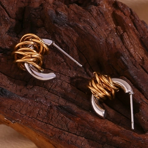 Macro detail of mixed gold and silver coiled C-shape stud earrings on a dark wood background