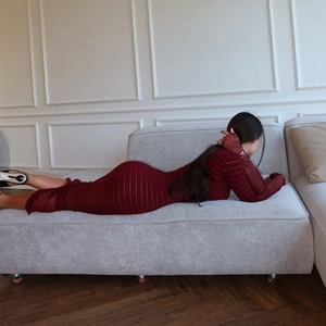 Detail eines burgunderfarbenen gestrickten Langarmkleids an einem Model auf dem Sofa