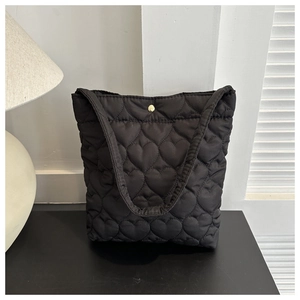Detailed view of heart-shaped quilted pattern and gold snap button on a black tote bag