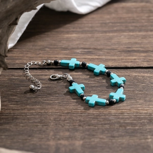 Detailed shot of turquoise cross bracelet with black beads on a rustic wooden surface