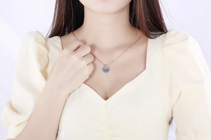 Detail of rose gold coin pendant necklace with blue enamel and zodiac pattern on model