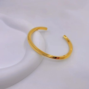 Detailed view of polished golden Mobius twist open bangle on white pedestal