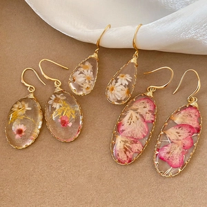 Detalle de pendientes hechos a mano de resina con flores reales y ganchos dorados
