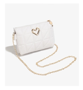 Detail of white quilted crossbody bag featuring a gold heart clasp and metal chain strap