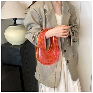 Detail of transparent orange acrylic box bag featuring elegant gold chain strap hardware