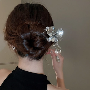 Detailed view of a silver floral hair stick with tassels worn in an elegant bun hairstyle
